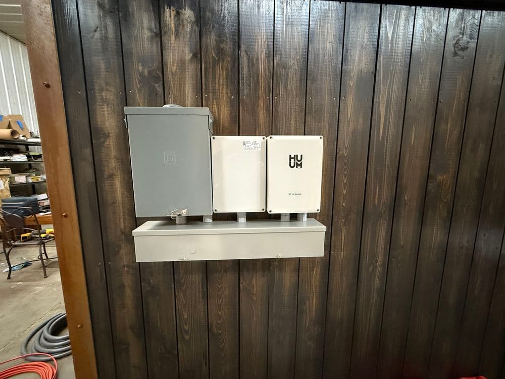 Control panel mounted on wooden wall in a workshop, featuring multiple electrical boxes.