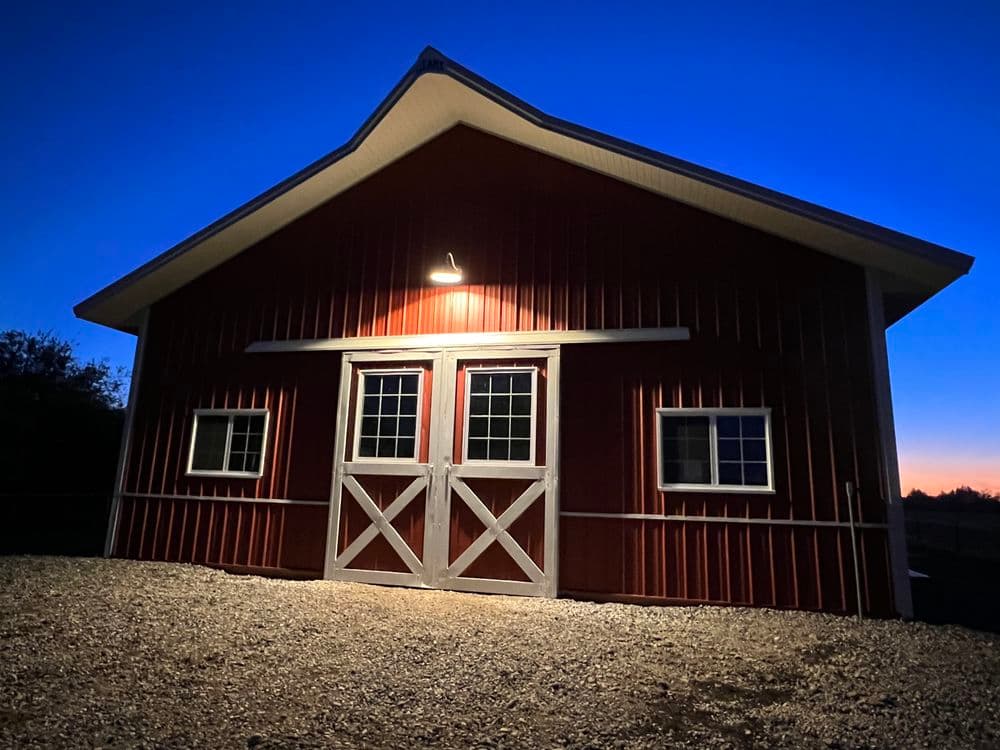 Red barn illuminated at dusk with blue sky, showcasing a modern design and rural charm.