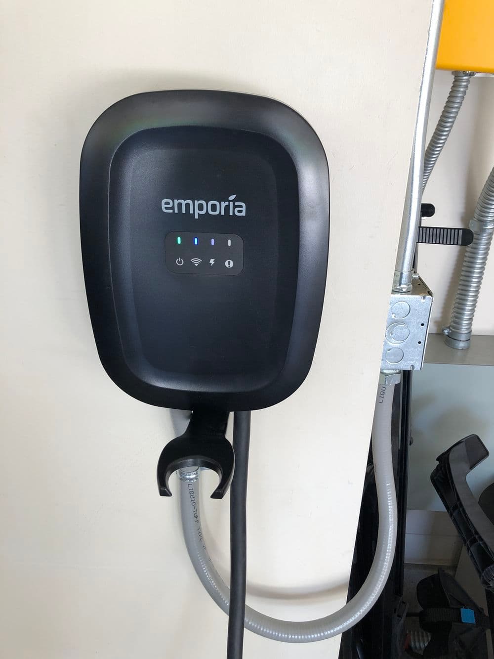 Emporia EV charger mounted on wall with cable connected, displaying charging status lights.