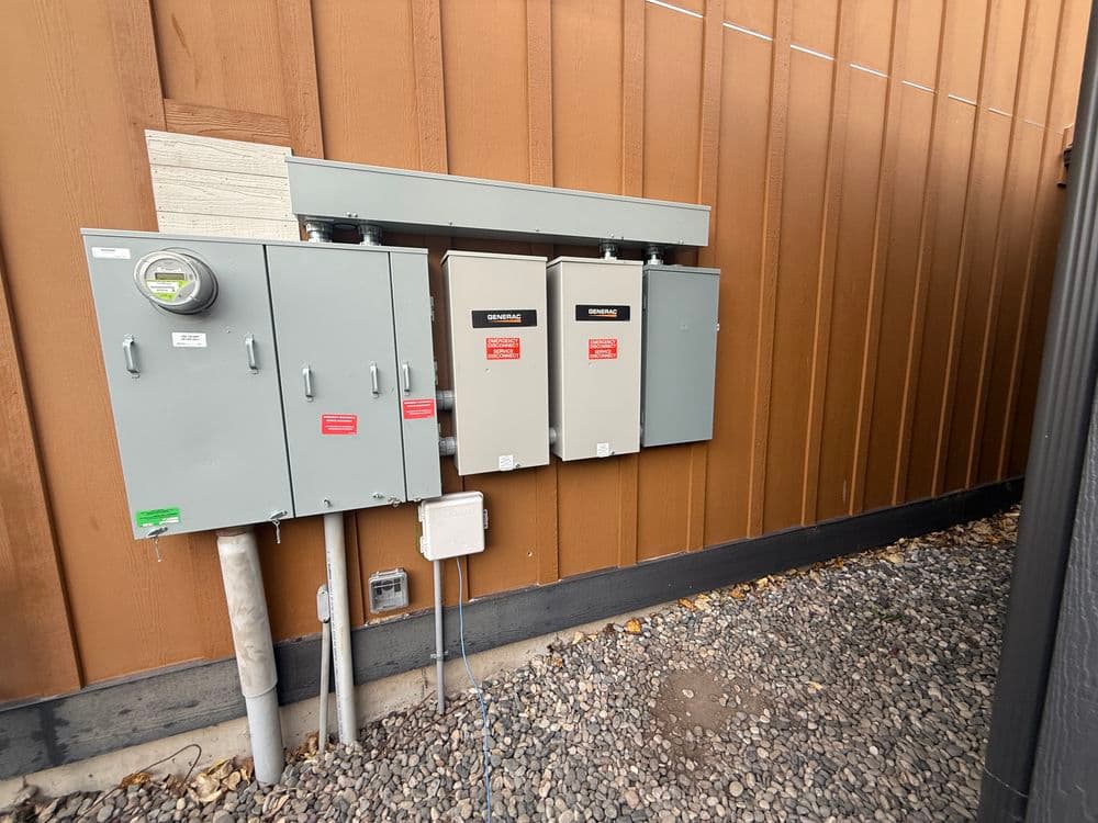 Electrical panel installation on a brown exterior wall with a gravel base.