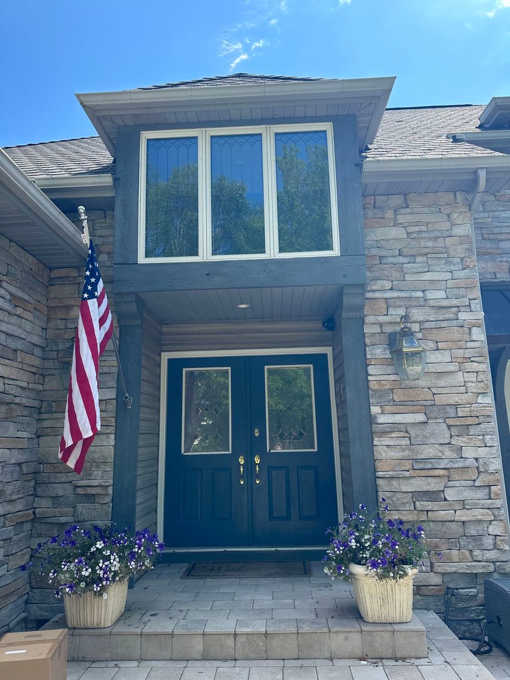 Elegant home entrance with double doors, stone exterior, American flag, and floral planters.