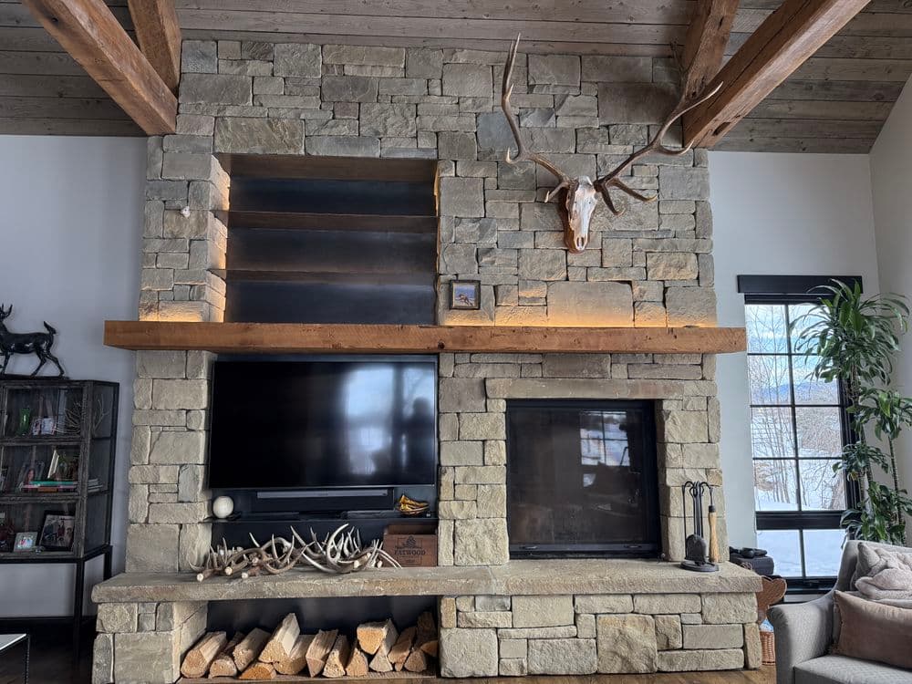 Modern stone fireplace with mounted deer skull, wood storage, and television in a stylish living room.