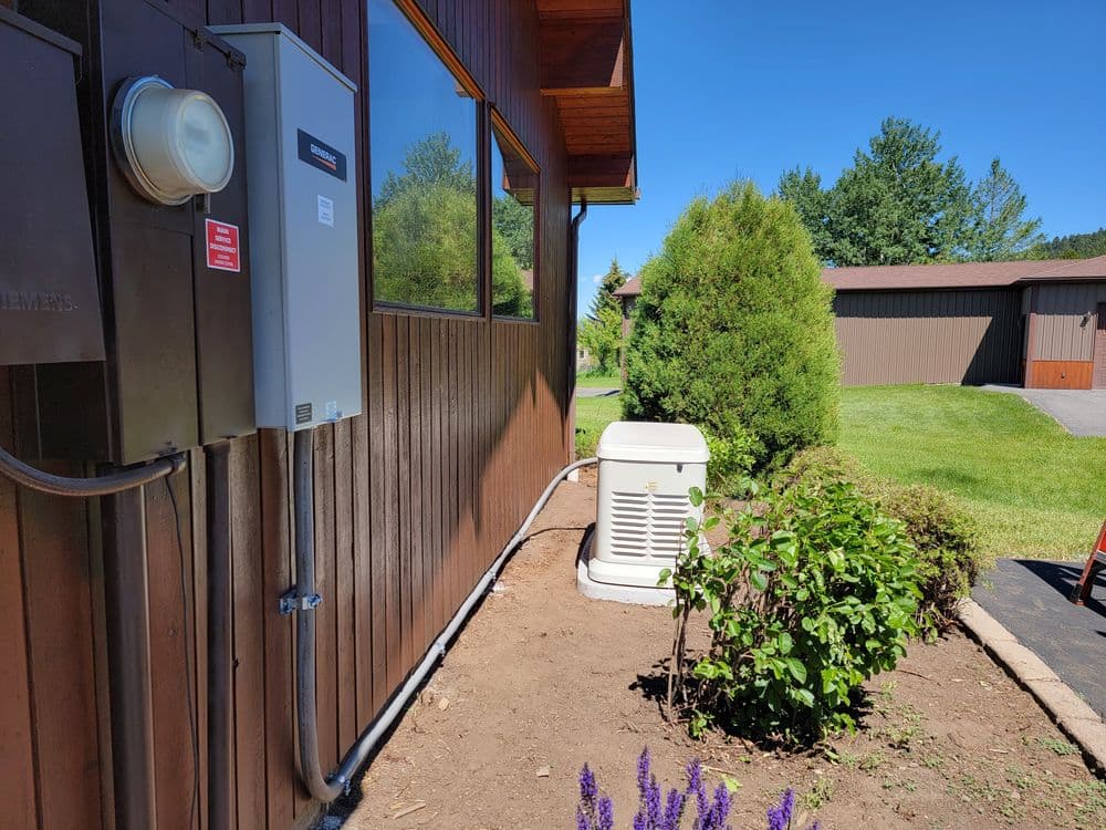 Generator installation beside a home, surrounded by landscaping and clear blue sky.