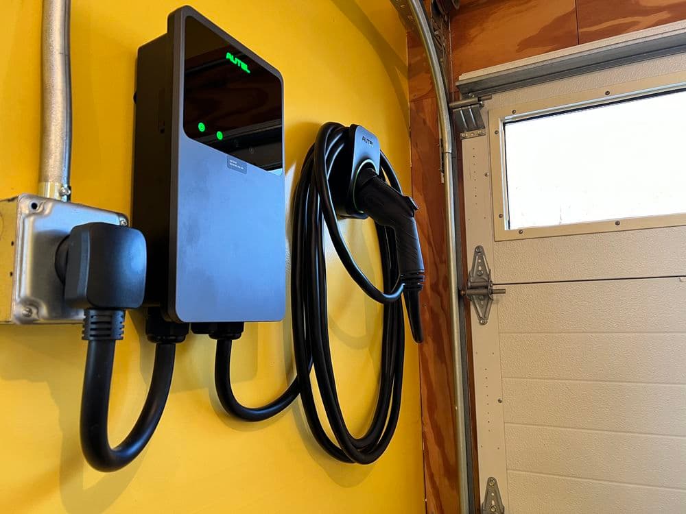 Electric vehicle charger mounted on a yellow wall, featuring a long charging cable and digital display.
