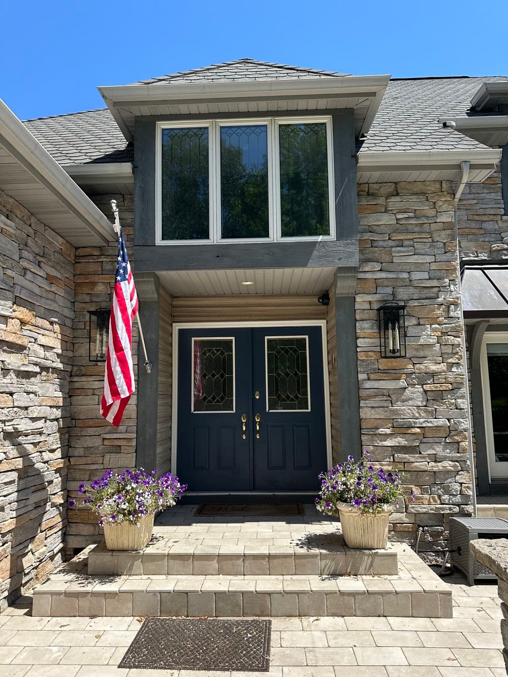 Charming stone house entrance with American flag and vibrant flower pots on a sunny day.