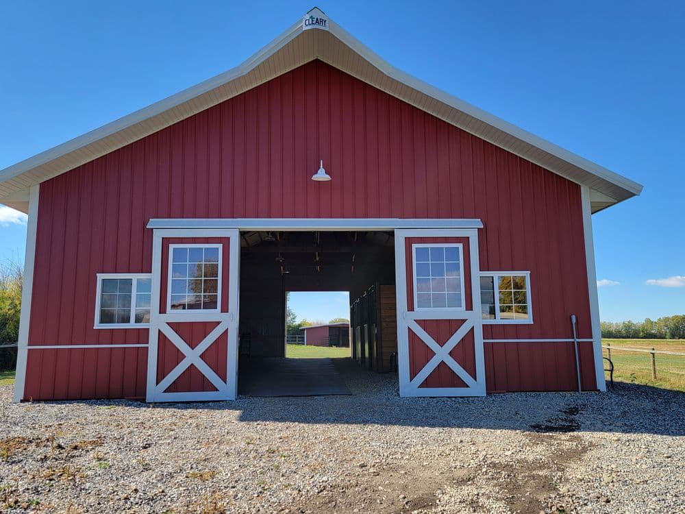 Red barn exterior with large open doors, gravel foreground, and blue sky in the background.