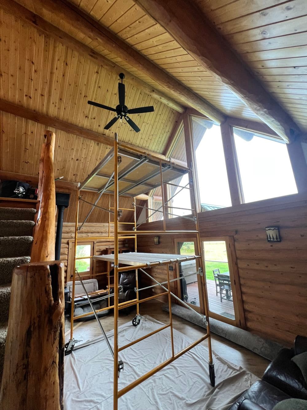 Scaffolding in a rustic wooden interior with large windows and a ceiling fan.