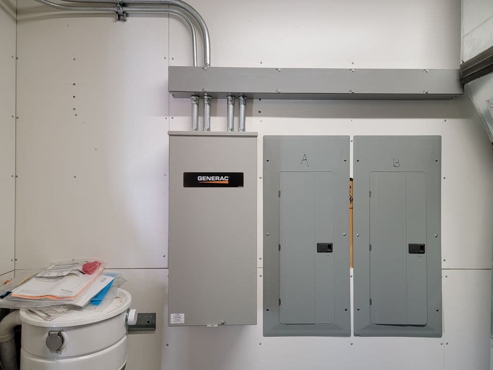 Generac generator with electrical panels mounted on a white wall in a utility room.