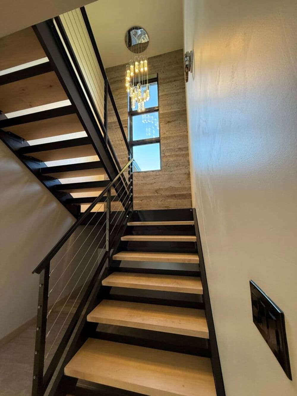 Modern staircase with wooden steps, metal railing, and contemporary chandelier.