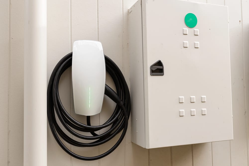 An electric vehicle charging station mounted on a wall next to a white electrical control panel.