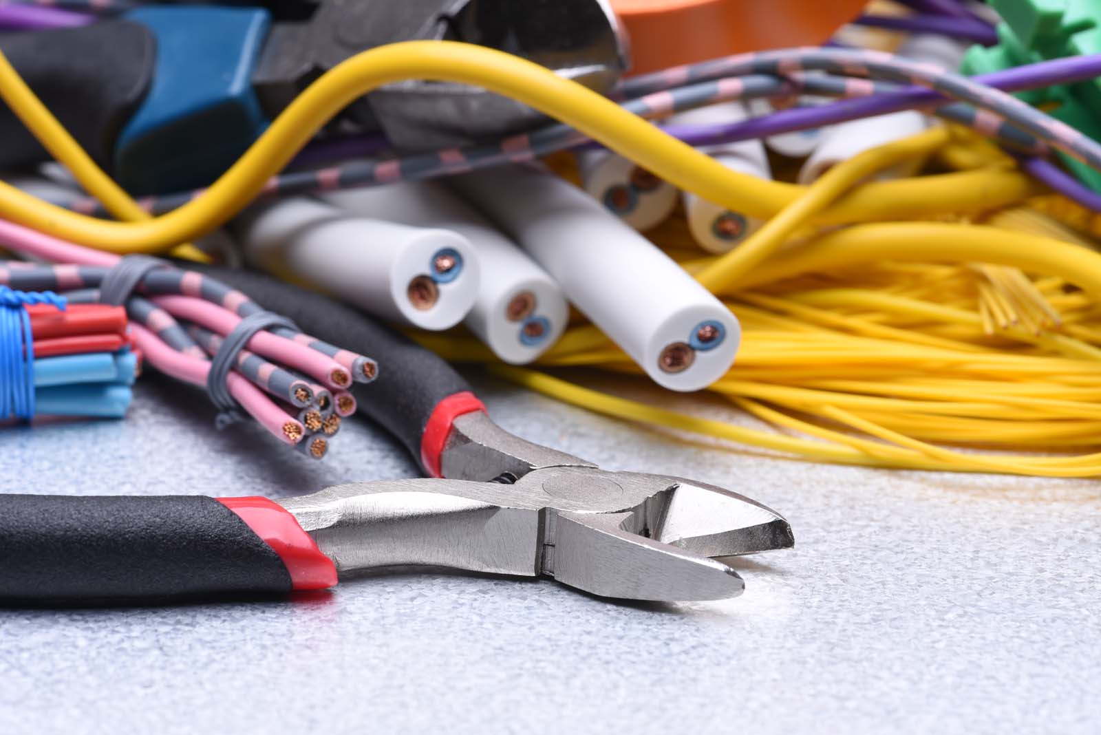 A pair of wire cutters lies on a surface next to bundled and loose electrical wires in various colors, ready for electrical repair tasks.