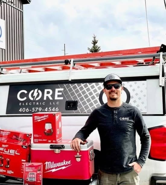 A man in sunglasses and a CORE Electric shirt stands next to Milwaukee tool boxes in front of a CORE Electric LLC work vehicle.